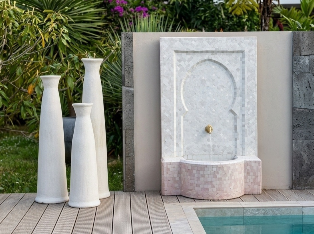 Une magnifique fontaine marocaine en zellige blanc sur une terrasse tropicale moderne, agrémentée de trois grands pots blancs au bord de la piscine