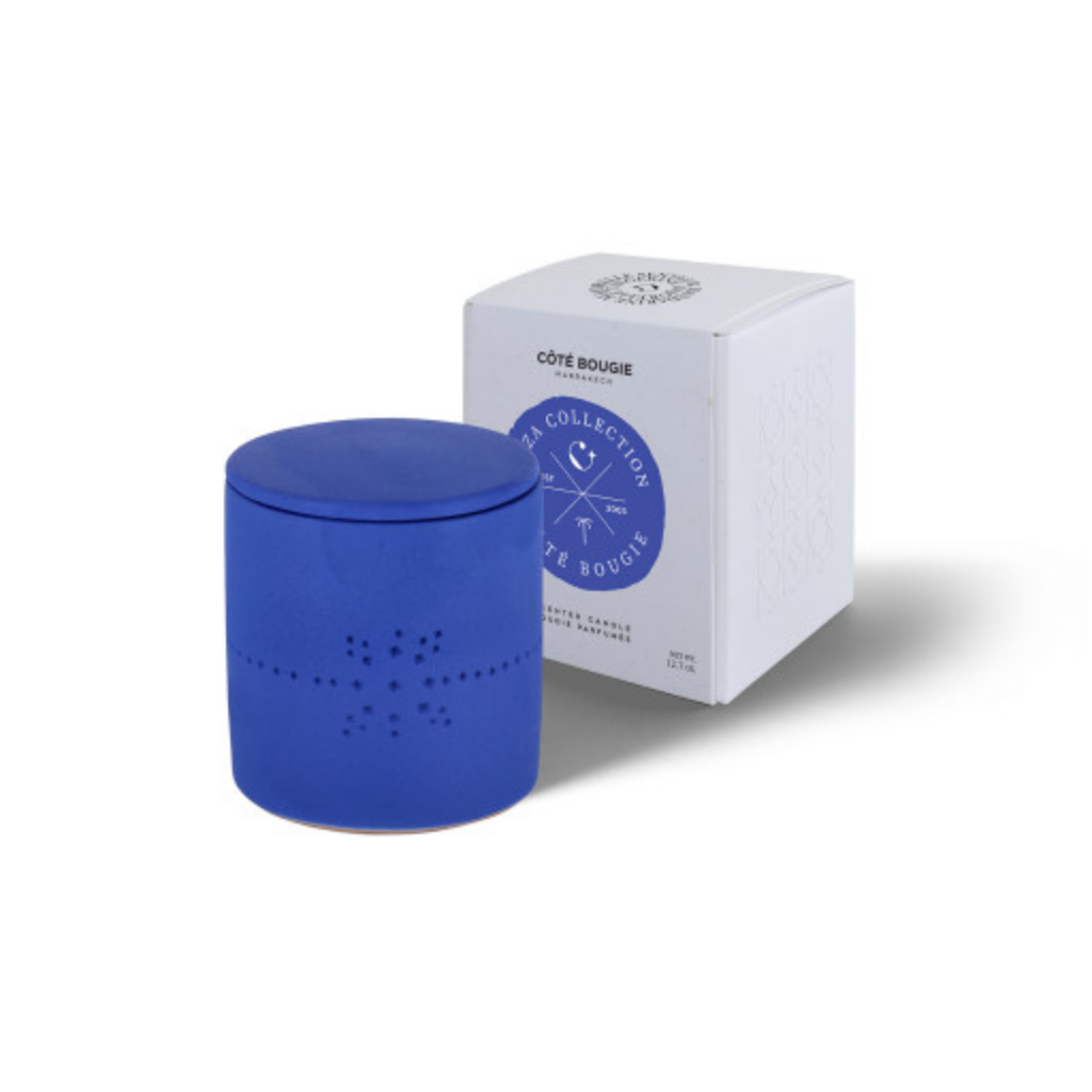 Bougie artisanale Izza Bleu et son coffret de Côté Bougie, senteur Mandarine Majorelle. Bougie en céramique bleue, façonnée à la main, posée à côté de son élégant coffret blanc illustré, mise en valeur sur fond blanc. Disponible à Majorelle Concept Store
