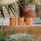 Photographie d'une bougie artisanale “Rue de la Liberté” de Côté Bougie, présentée dans un pot en terre cuite naturelle avec une étiquette gravée. La bougie est posée sur une table en bois, entourée d'éléments de décoration marocains, créant une ambiance chaleureuse et authentique.