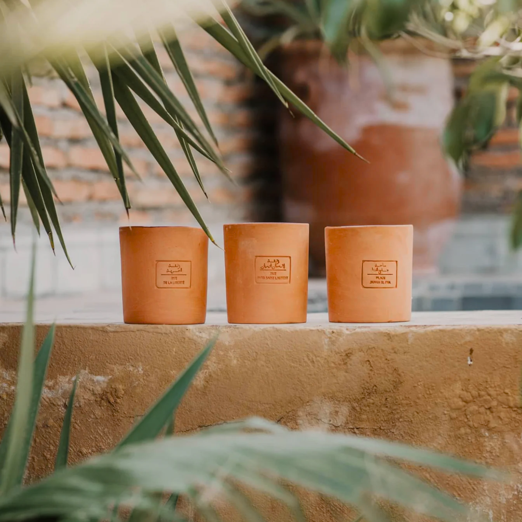 Photographie d'une bougie artisanale “Rue de la Liberté” de Côté Bougie, présentée dans un pot en terre cuite naturelle avec une étiquette gravée. La bougie est posée sur une table en bois, entourée d'éléments de décoration marocains, créant une ambiance chaleureuse et authentique.