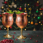 Duo de verres à cocktail sur pied en cuivre satiné remplis de grenade et menthe, ambiance Noël chic chez Majorelle.