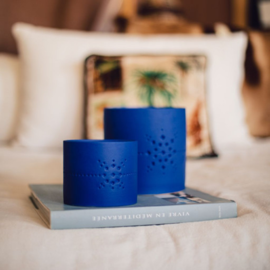 Bougies Izza Bleu de Côté Bougie, senteur Mandarine Majorelle, disposées sur un livre dans une chambre à la décoration chaleureuse. Scène lifestyle mettant en avant l’élégance de la céramique bleue et l’ambiance cocooning, idéale pour illustrer l’intégration de la bougie dans un intérieur raffiné. Disponible à Majorelle concept store marocain
