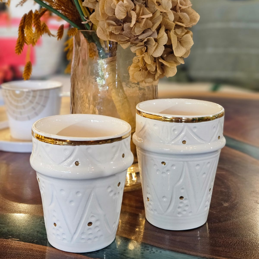 Tasse beldi artisanale blanche, décor sculpté et bordure dorée, présentée seule ou en duo sur une table de bois, ambiance florale et chic. Parfaite pour le thé, le café ou en objet déco.