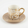 Tasse en porcelaine blanche avec anse dorée et calligraphie arabe dorée en relief sur soucoupe assortie.