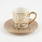 Tasse en porcelaine blanche avec anse dorée et calligraphie arabe dorée en relief sur soucoupe assortie.
