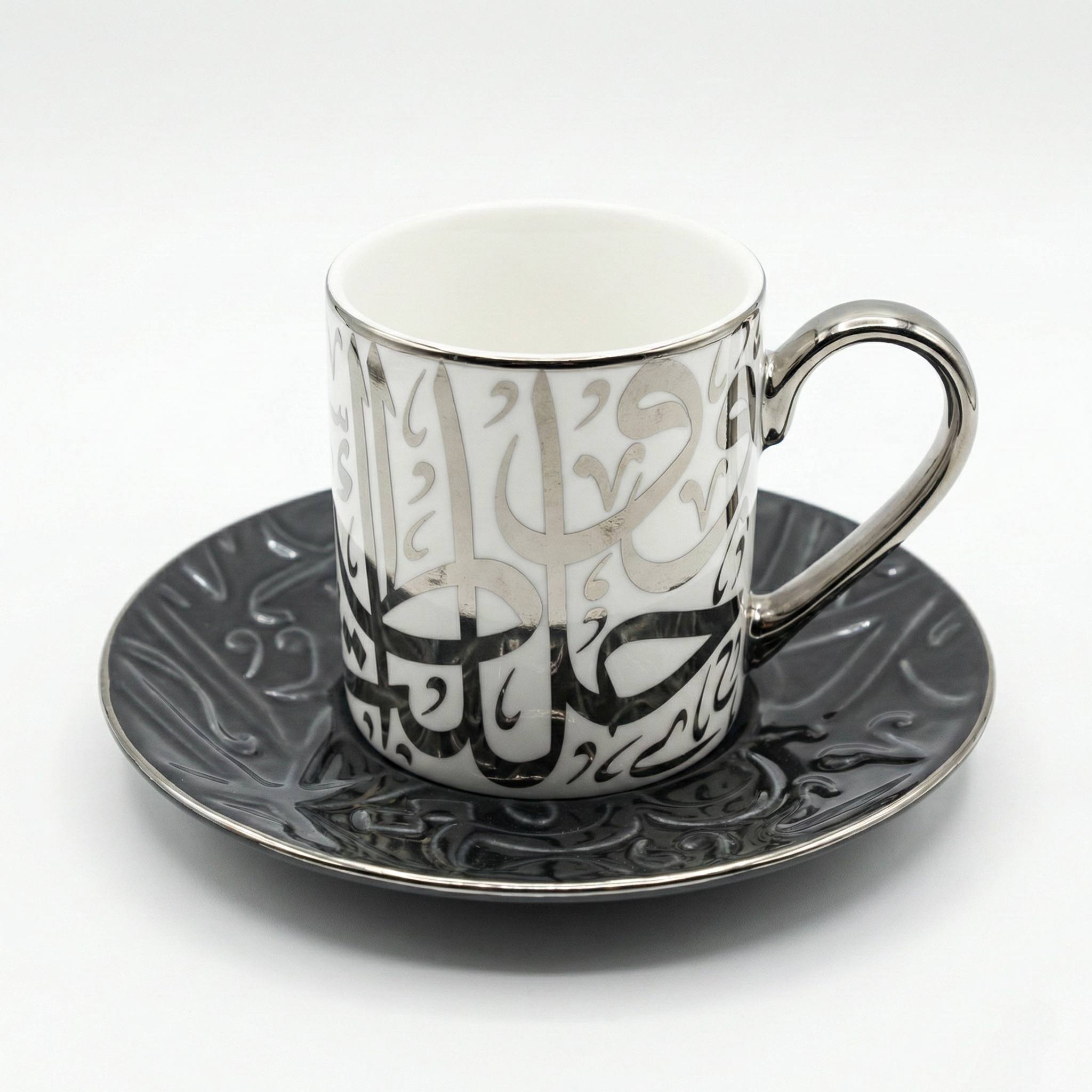 Ensemble tasse blanche et soucoupe noire avec calligraphie arabe argentée en relief.
