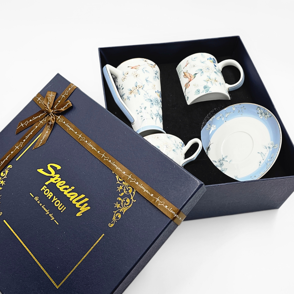 Boîte cadeau ouverte contenant trois pièces en porcelaine décorées d’oiseaux et de fleurs.