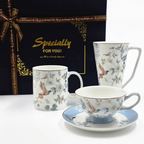Ensemble en porcelaine avec motifs oiseaux et fleurs devant un coffret cadeau bleu nuit.