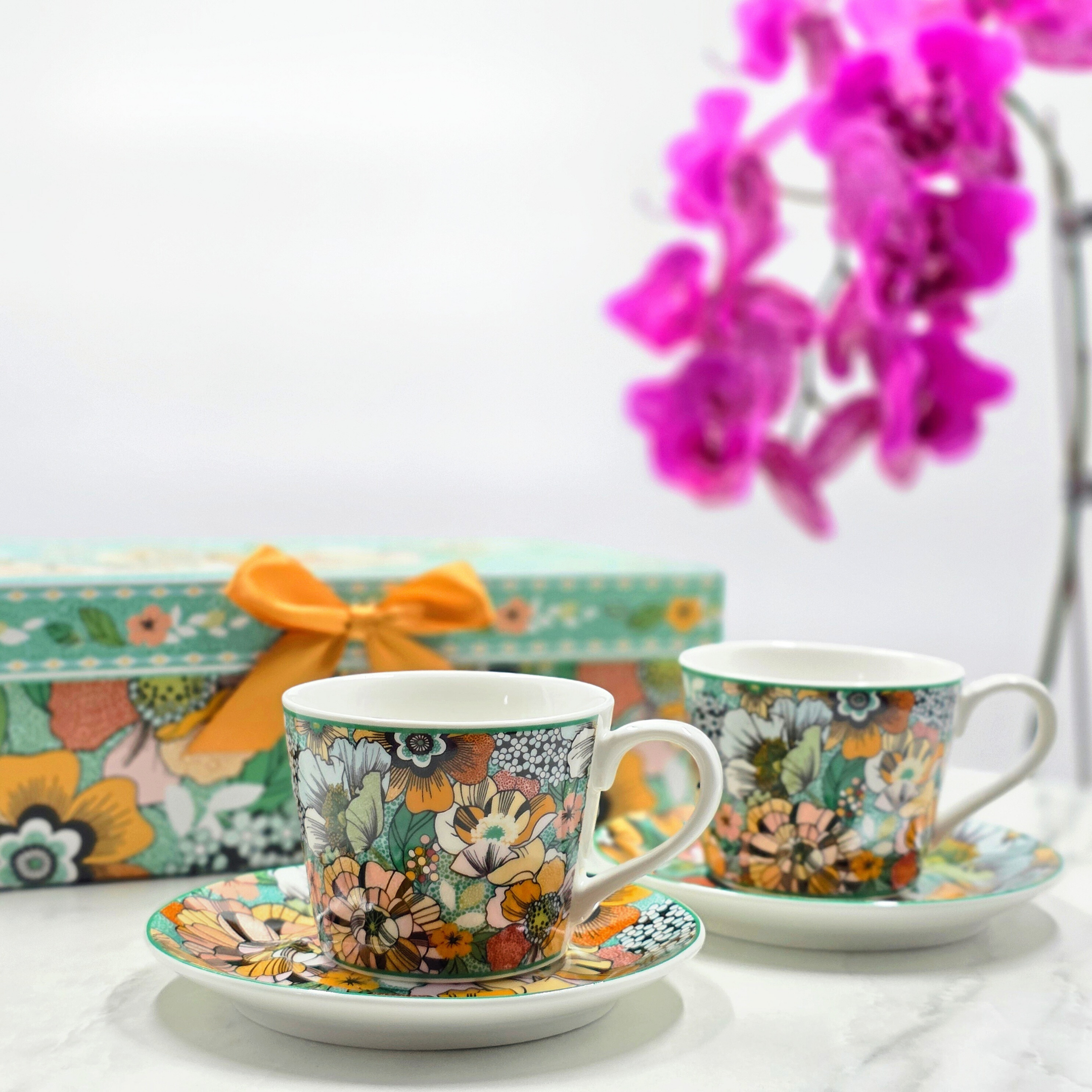 Tasses en porcelaine florale avec sous-tasses, présentées devant un coffret cadeau assorti, collection Fêtes de Fin d’Année Majorelle.