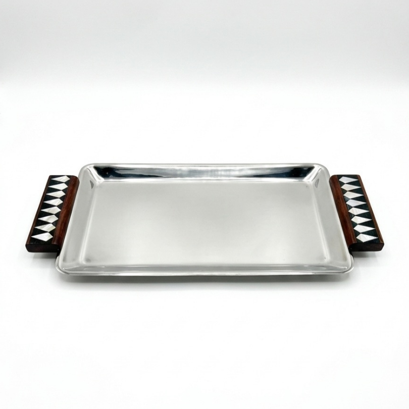 Plateau de service rectangulaire en acier poli miroir avec anses en bois et marqueterie de losanges noirs et blancs.