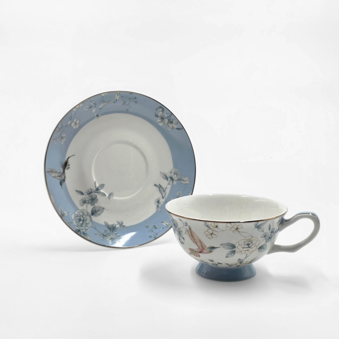 Tasse et soucoupe en porcelaine bleu pastel avec motifs oiseaux et fleurs.