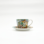 Tasse en porcelaine avec motifs floraux colorés, posée sur sa sous-tasse, fond blanc.