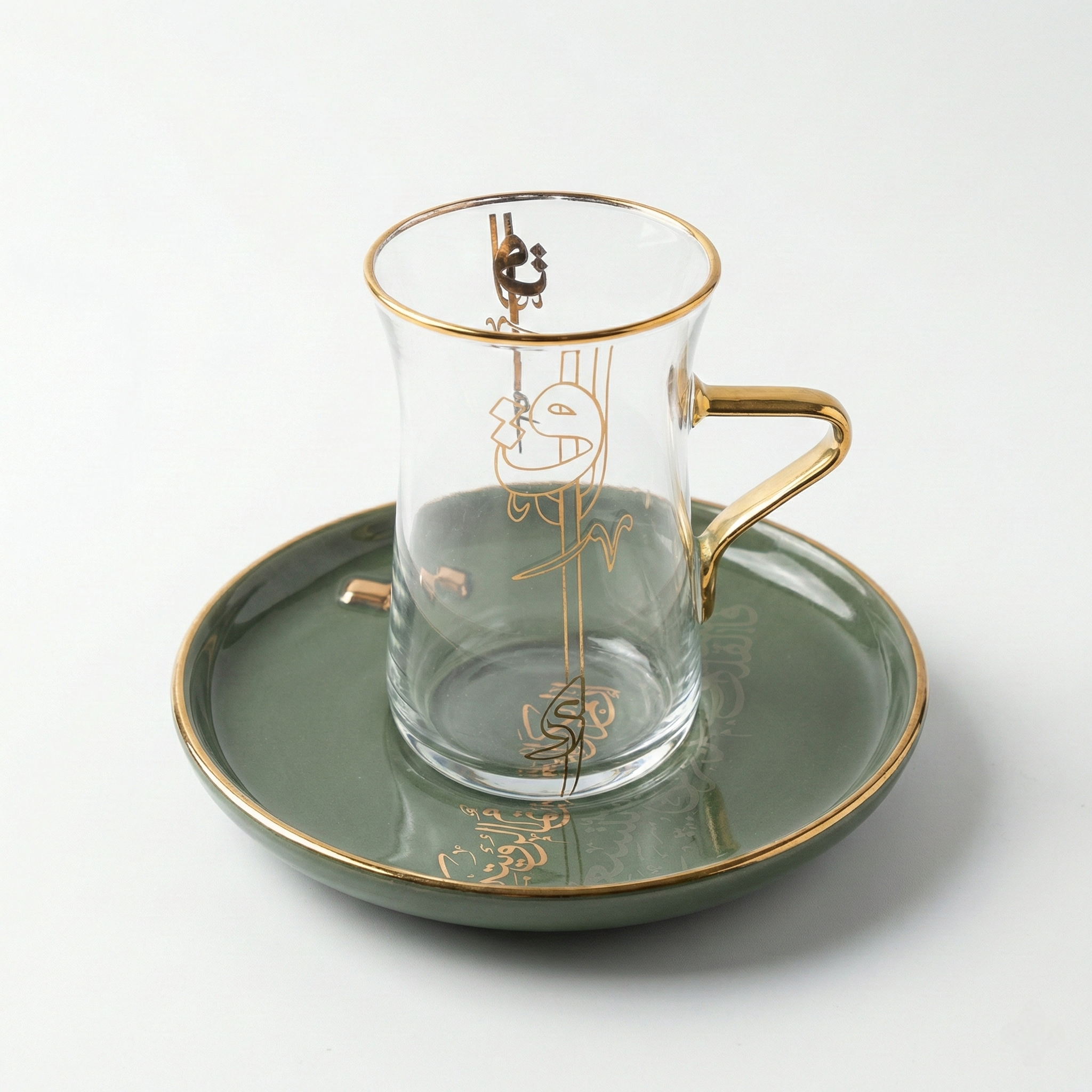 Verre à thé transparent avec anse dorée et soucoupe en porcelaine vert émeraude à motifs calligraphiques dorés.